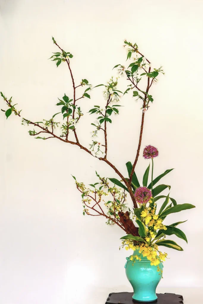 Composition d’ikebana avec fleurs et branches dans un vase turquoise